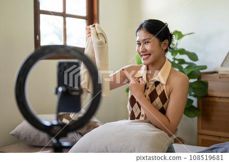 A charming female influencer or online seller is showing and reviewing her clothes to the camera. A charming female influencer or online seller is showing and reviewing her clothes to the camera. 108519681
