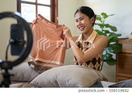 A beautiful female influencer or online seller is showing and reviewing her clothes to the camera. A beautiful female influencer or online seller is showing and reviewing her clothes to the camera. 108519682