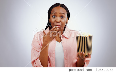 Portrait, surprise or black woman watching movie in studio for cinema with popcorn to relax. Omg, wow or shocked African person eating snack for streaming film or subscription on grey background Portrait, surprise or black woman watching movie in studio for cinema with popcorn to relax. Omg, wow or shocked African person eating snack for streaming film or subscription on grey background 108520078