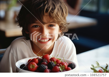 The boy is sitting at the table with a berry plate 108521757