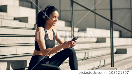 Runner woman, headphones and phone on stairs with music, smile and relax in city, workout and training. Girl, smartphone and happy with audio streaming subscription with typing, social media or app 108521897