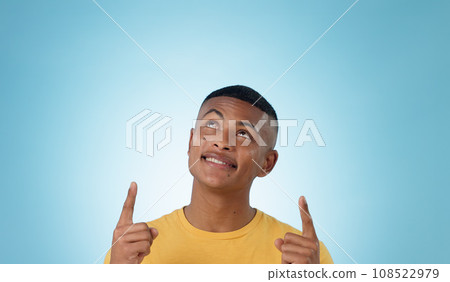 Man, space and pointing up in studio for advertising choice, decision and information about us on blue background. Face, model and thinking to show presentation of mockup, promotion and announcement Man, space and pointing up in studio for advertising choice, decision and information about us on blue background. Face, model and thinking to show presentation of mockup, promotion and announcement 108522979