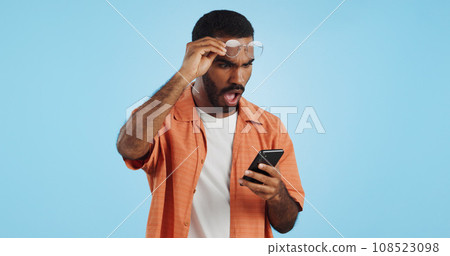 Man, smartphone and surprise announcement with shock, facial expression and drama online on blue background. Wow, reaction to news on social media and communication, mobile app and alarm in studio Man, smartphone and surprise announcement with shock, facial expression and drama online on blue background. Wow, reaction to news on social media and communication, mobile app and alarm in studio 108523098