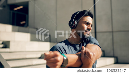 Fitness, headphones and man stretching arms on stairs in city, workout and exercise for body health. Music, serious athlete and person warm up on steps in urban town, listening to audio and thinking 108523247