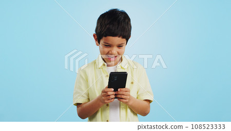Kid, phone or typing to chat in studio on social media to play mobile games or download app. Blue background, scroll or boy child reading notification for online communication or watch fun multimedia Kid, phone or typing to chat in studio on social media to play mobile games or download app. Blue background, scroll or boy child reading notification for online communication or watch fun multimedia 108523333