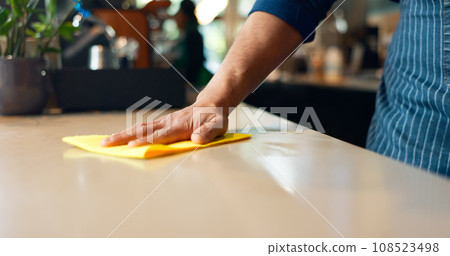 Waiter, hands and cleaning table in coffee shop for dust, bacteria and dirt with cloth, spray or detergent. Barista, person and wipe wooden furniture in cafe or restaurant for shine or professional 108523498