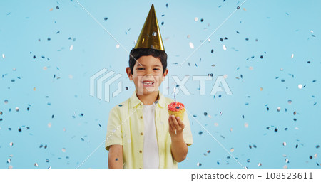 Happy birthday, child and portrait with confetti in party with cupcake, hat and happiness in studio blue background. Congratulations, kid and boy with cake, glitter and smile on face for magic event 108523611
