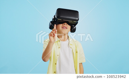 VR, child and glasses with video gaming, technology and metaverse online in studio. Young boy, gamer and augmented reality app for streaming and virtual graphic on internet with blue background 108523942