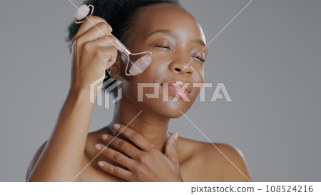 Black woman, face with roller and massage for beauty and skincare, natural cosmetics and treatment on white background. Wellness, dermatology and skin glow, rose quartz crystal and tools in studio 108524216