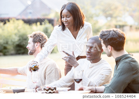 Cheers to Friendship: Hostess Pours Wine at Multiracial Garden Dinner Party 108524404