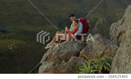 Hiking, mountain and love, couple relax on outdoor adventure and peace in nature with romance. Trekking, rock climbing and view, man and woman with view of natural landscape sitting on cliff together 108525405