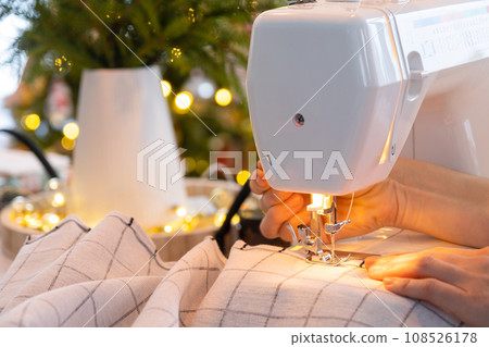 Sewing process on a sewing machine, women hands control needle with a thread white checkered fabric. Preparation for Christmas and new year, textiles for cozy in festive decor interior 108526178