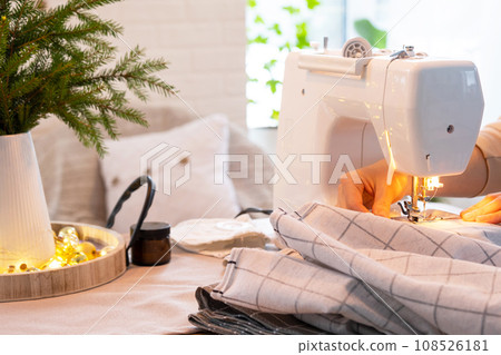 Sewing process on a sewing machine, women hands control needle with a thread white checkered fabric. Preparation for Christmas and new year, textiles for cozy in festive decor interior 108526181