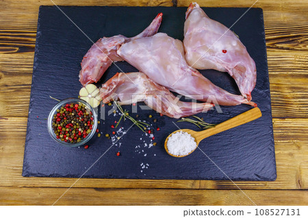 Raw rabbit legs with spices on a black slate cutting board on wooden table. Top view 108527131