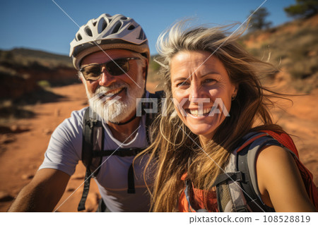 Elderly smiling couple in safety helmets riding bicycles together to stay fit and healthy. Caucasian seniors having fun on a bike ride in summer countryside. Retired people lead active lifestyle. Elderly smiling couple in safety helmets riding bicycles together to stay fit and healthy. Caucasian seniors having fun on a bike ride in summer countryside. Retired people lead active lifestyle. 108528819