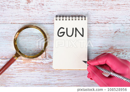 GUN writing on a notebook lying on old boards next to a magnifying glass and a hand in a red medical glove with a pencil 108528956