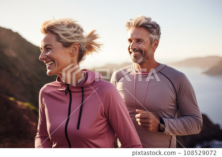 Athletic adult couple jogging along the picturesque seashore. Mature slender Caucasian man and woman in sports outfit having fun and smiling while running. Active lifestyle for all ages. Athletic adult couple jogging along the picturesque seashore. Mature slender Caucasian man and woman in sports outfit having fun and smiling while running. Active lifestyle for all ages. 108529072