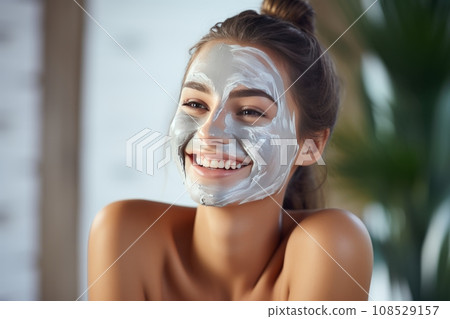 Close-up portrait of beautiful smiling girl in spa studio applying facial mask on her face. Spa beauty procedures applying nourishing facial clay mask. Beauty treatment and skin care. Close-up portrait of beautiful smiling girl in spa studio applying facial mask on her face. Spa beauty procedures applying nourishing facial clay mask. Beauty treatment and skin care. 108529157