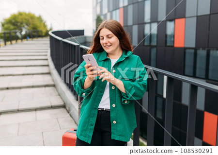 Young woman with a red suitcase using smart phone at airport. Redhead girl in international airport walking with her luggage. Concept of travel 108530291