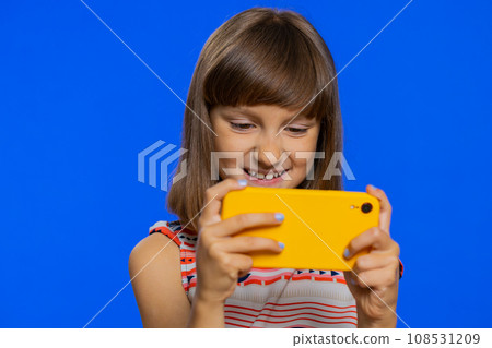 Preteen child kid girl enthusiastically playing racing or shooter video games on smartphone app 108531209