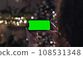 Woman Holding in Hands Cellphone Green Screen in Holidays Decoration Back View Close up. Young Person Relaxing Home and Looking at Device. Resting Sitting and Blank Gadget 4k 108531348