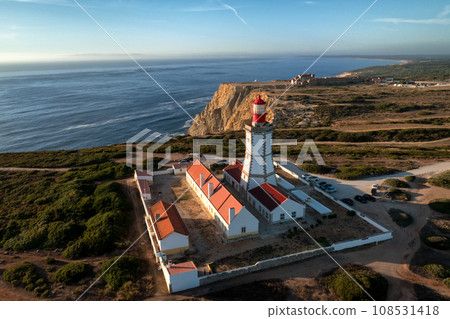 Beautiful drone view of lighthouse on Cabo Espichel or cape Espichel at sunset. Atlantic ocean coast, Sesimbra, Portugal. Seashores, high cliffs, Portuguese architecture, sunset summer landscape, blue Beautiful drone view of lighthouse on Cabo Espichel or cape Espichel at sunset. Atlantic ocean coast, Sesimbra, Portugal. Seashores, high cliffs, Portuguese architecture, sunset summer landscape, blue 108531418