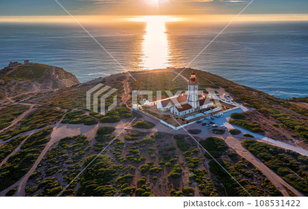 Beautiful view of traditional lighthouse on Cabo Espichel or cape Espichel at sunset. Atlantic ocean coast, Sesimbra, Portugal. Seashores, high cliffs, Portuguese architecture, sunset summer landscape Beautiful view of traditional lighthouse on Cabo Espichel or cape Espichel at sunset. Atlantic ocean coast, Sesimbra, Portugal. Seashores, high cliffs, Portuguese architecture, sunset summer landscape 108531422