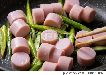 A cooking scene of frying garlic sprouts and fish sausage in a frying pan. 108532097