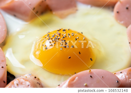 A cooking scene where fried eggs (with black pepper) and fish sausage are fried in a frying pan. A cooking scene where fried eggs (with black pepper) and fish sausage are fried in a frying pan. 108532148