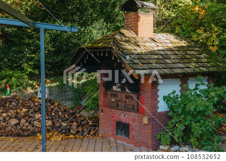 An Old Stove And Firewood For It In The Yard In The Village. Old Stone Fireplace Outdoors In The Fall. Traditional Brick Oven With Wood For Baking Bread Outdoor In Europe. An Old Stove And Firewood For It In The Yard In The Village. Old Stone Fireplace Outdoors In The Fall. Traditional Brick Oven With Wood For Baking Bread Outdoor In Europe. 108532652