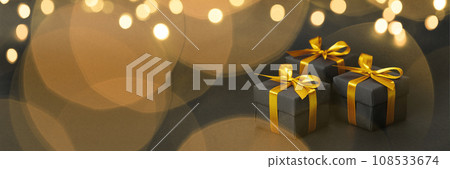 Black gift box with golden ribbon bow on black background 108533674