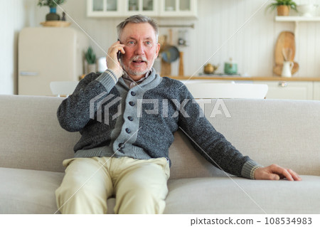 Happy middle aged senior man talking on smartphone with family friends. Older mature grandfather with cell phone talking with grown up children, resting at home. Older generation modern tech usage Happy middle aged senior man talking on smartphone with family friends. Older mature grandfather with cell phone talking with grown up children, resting at home. Older generation modern tech usage 108534983