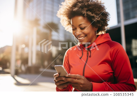 Young athletic African American woman in sportswear with smartphone while training outdoor. Slender black lady resting after jogging or workout in city street. Active lifestyle in urban environment. Young athletic African American woman in sportswear with smartphone while training outdoor. Slender black lady resting after jogging or workout in city street. Active lifestyle in urban environment. 108535345