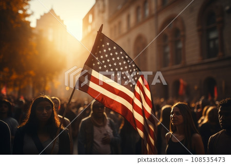 A huge crowd of people marches along a city street with American flags. The Stars and Stripes flutter over people's heads. Independence Day 4th of July concept. The US main holiday. National pride. A huge crowd of people marches along a city street with American flags. The Stars and Stripes flutter over people's heads. Independence Day 4th of July concept. The US main holiday. National pride. 108535473