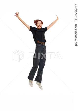 Happy, smiling young woman wearing casual black cloth raised hands while jumping on white studio background. 108536014