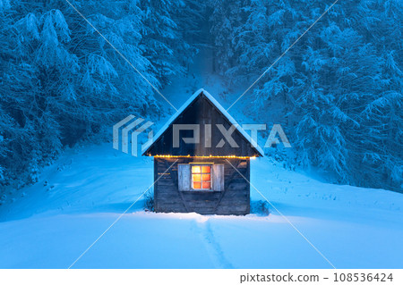 A quiet wooden cabin standing alone in a snow-covered mountain meadow A quiet wooden cabin standing alone in a snow-covered mountain meadow 108536424
