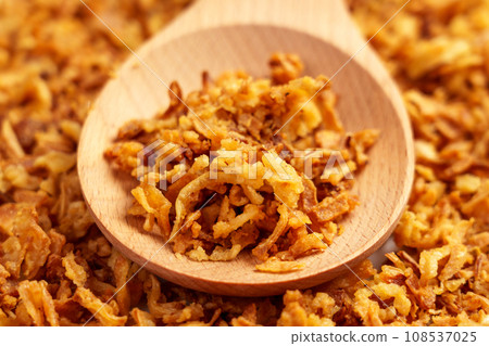 Crispy fried onions in wooden spoon. Roasted golden shallot flakes.  108537025