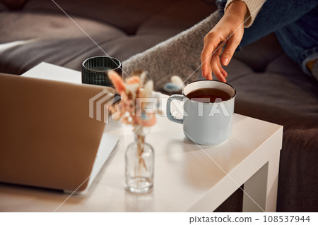 Woman's delicate hand reaches for cup of hot fragrant tea standing on coffee table at home. Relaxing atmosphere. 108537944