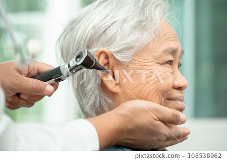 Audiologist or ENT doctor use otoscope checking ear of asian senior woman patient treating hearing loss problem. 108538962