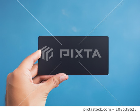 Male hand holding a black bank card on a blue background AI 108539625
