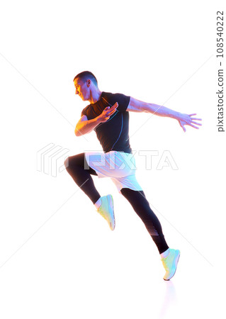 Full-length dynamic image of young man in sportswear training, running against white studio background in neon light Full-length dynamic image of young man in sportswear training, running against white studio background in neon light 108540222