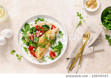 Omelette stuffed with tomato, broccoli, feta cheese and fresh green leaves of arugula and spinach. Healthy diet food, breakfast. Top view Omelette stuffed with tomato, broccoli, feta cheese and fresh green leaves of arugula and spinach. Healthy diet food, breakfast. Top view 108540347