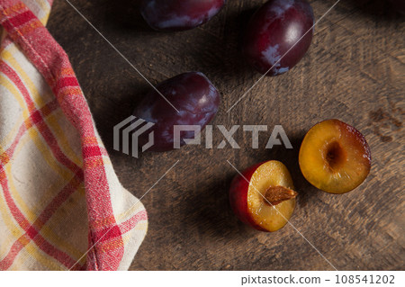 Whole and half of purple plums on wooden background. . 108541202