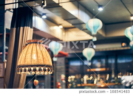 Vintage floor lamp with yellow light on the background of hanging lamps in the restaurant in the evening. The floor lamp is reflected in a dark window where there is a place to copy.High quality photo 108541483