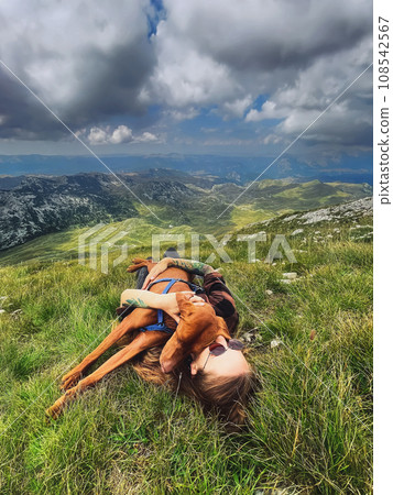 Woman with Vizsla Dog Lying on Mountain Top 108542567
