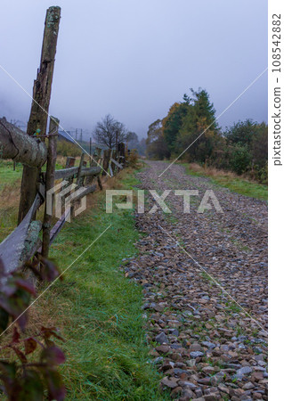 Road in the countryside. Morning foggy pathway in Carpathian village. Footpath in autumn field with fence. Rural dirty road in morning mist in perspective. November magic landscape in village. Road in the countryside. Morning foggy pathway in Carpathian village. Footpath in autumn field with fence. Rural dirty road in morning mist in perspective. November magic landscape in village. 108542882