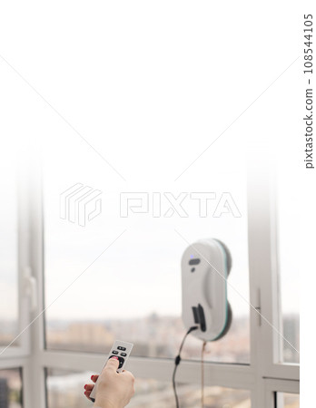 Woman washing  and cleaning windows  with smart vacuum cleaner. Using remote controller 108544105