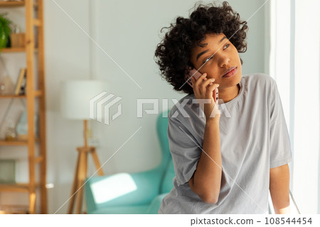 African american girl talking on smartphone at home indoor. Young woman with cell phone chatting with friends. Smiling teen girl making answering call by cellphone. Lady having conversation by mobile African american girl talking on smartphone at home indoor. Young woman with cell phone chatting with friends. Smiling teen girl making answering call by cellphone. Lady having conversation by mobile 108544454