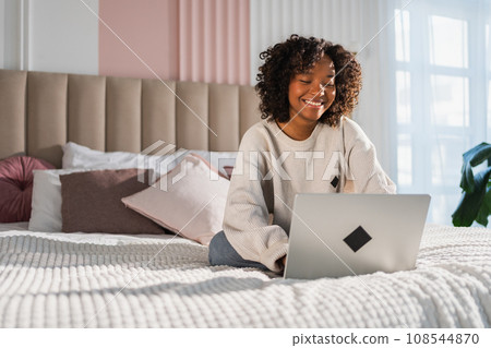 African American girl using laptop in bed at home office typing chatting reading writing email. Young black woman having virtual meeting online chat video call conference. Work learning from home 108544870