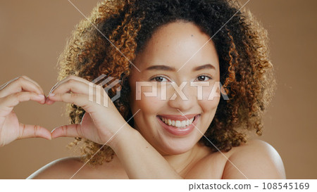 Portrait of happy woman, heart hands or natural beauty dermatology for wellness in studio with smile. Skin glow, skincare or proud biracial female person with self love gesture on brown background Portrait of happy woman, heart hands or natural beauty dermatology for wellness in studio with smile. Skin glow, skincare or proud biracial female person with self love gesture on brown background 108545169